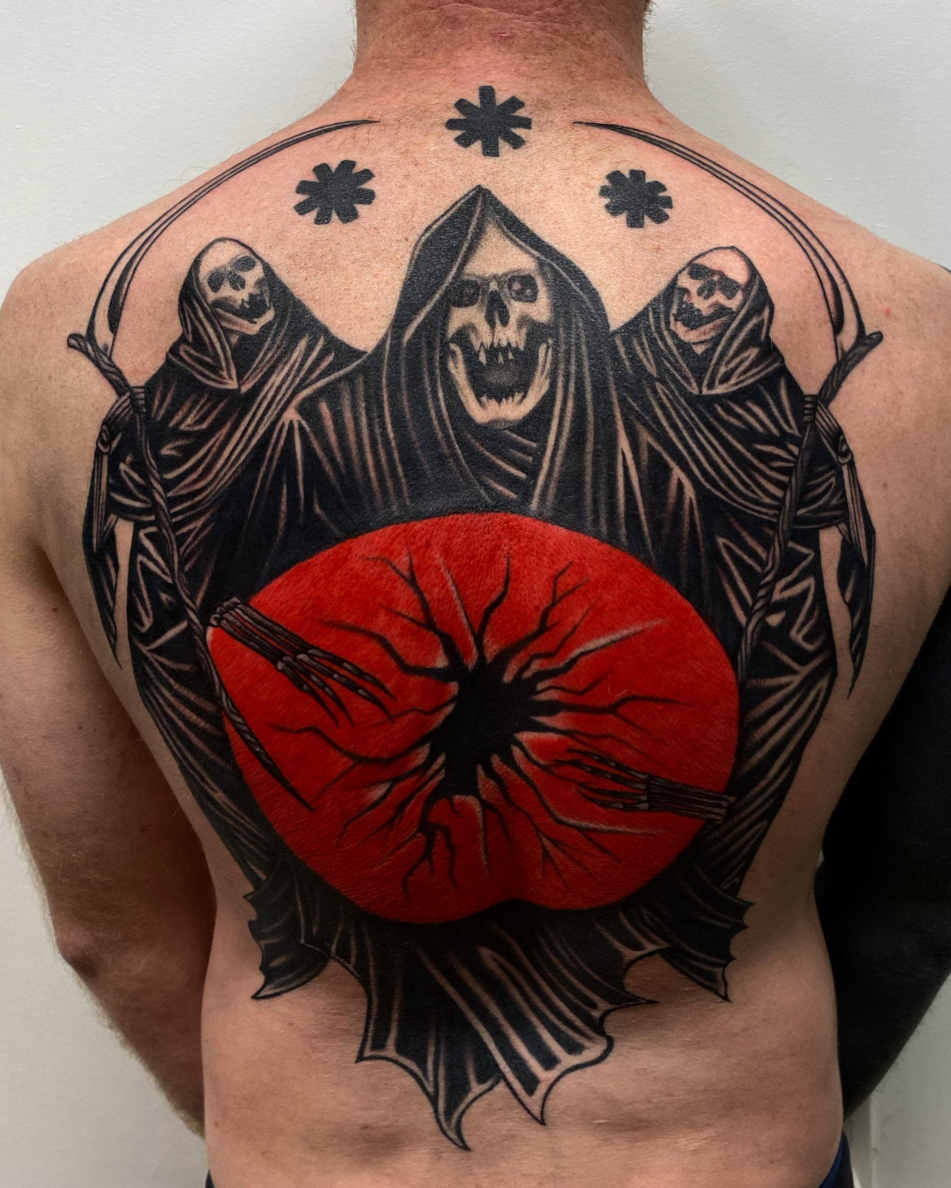 Three hooded reapers holding scythes around a cracked red moon across the upper back